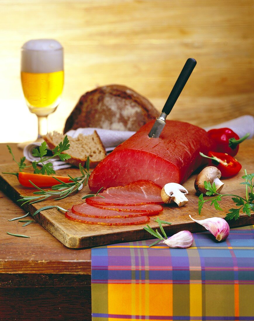 Beef ham on chopping board; mushrooms, bread, beer