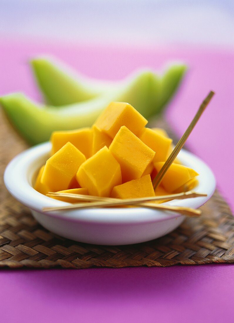 Diced mango in bowl in front of slices of melon