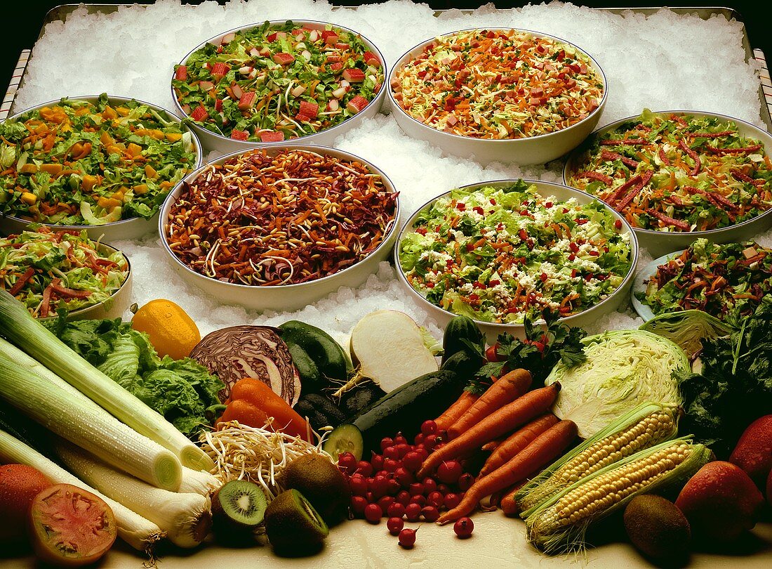 Verschiedene Salate in Schüsseln auf Eis und frisches Gemüse