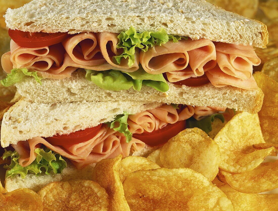 Sandwich mit Schinken, Tomaten und Salatblatt, daneben Chips