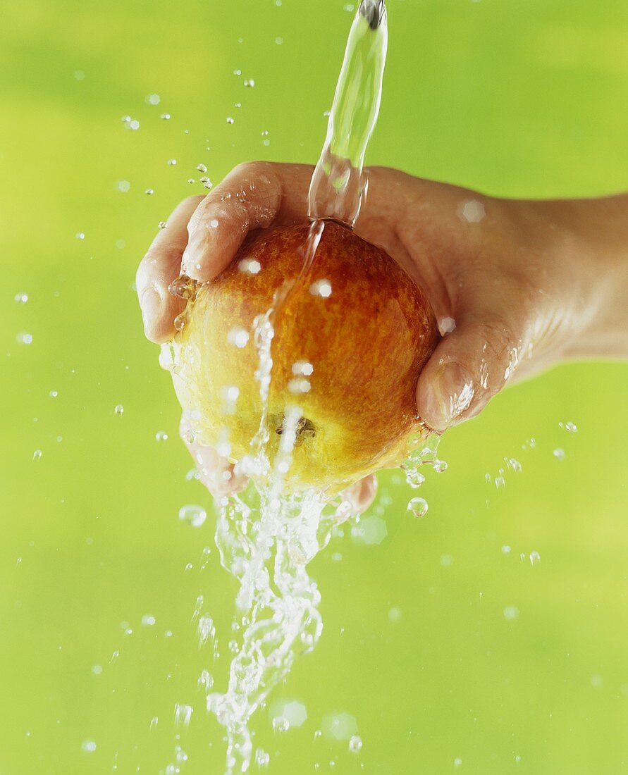 Hand hält Apfel unter fliessendes Wasser