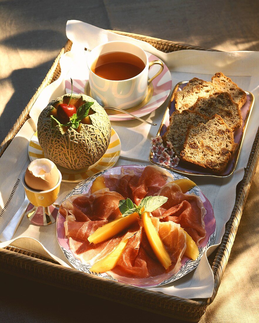 Frühstück mit Schinken, Melone, Ei, Früchtebrot und Tee