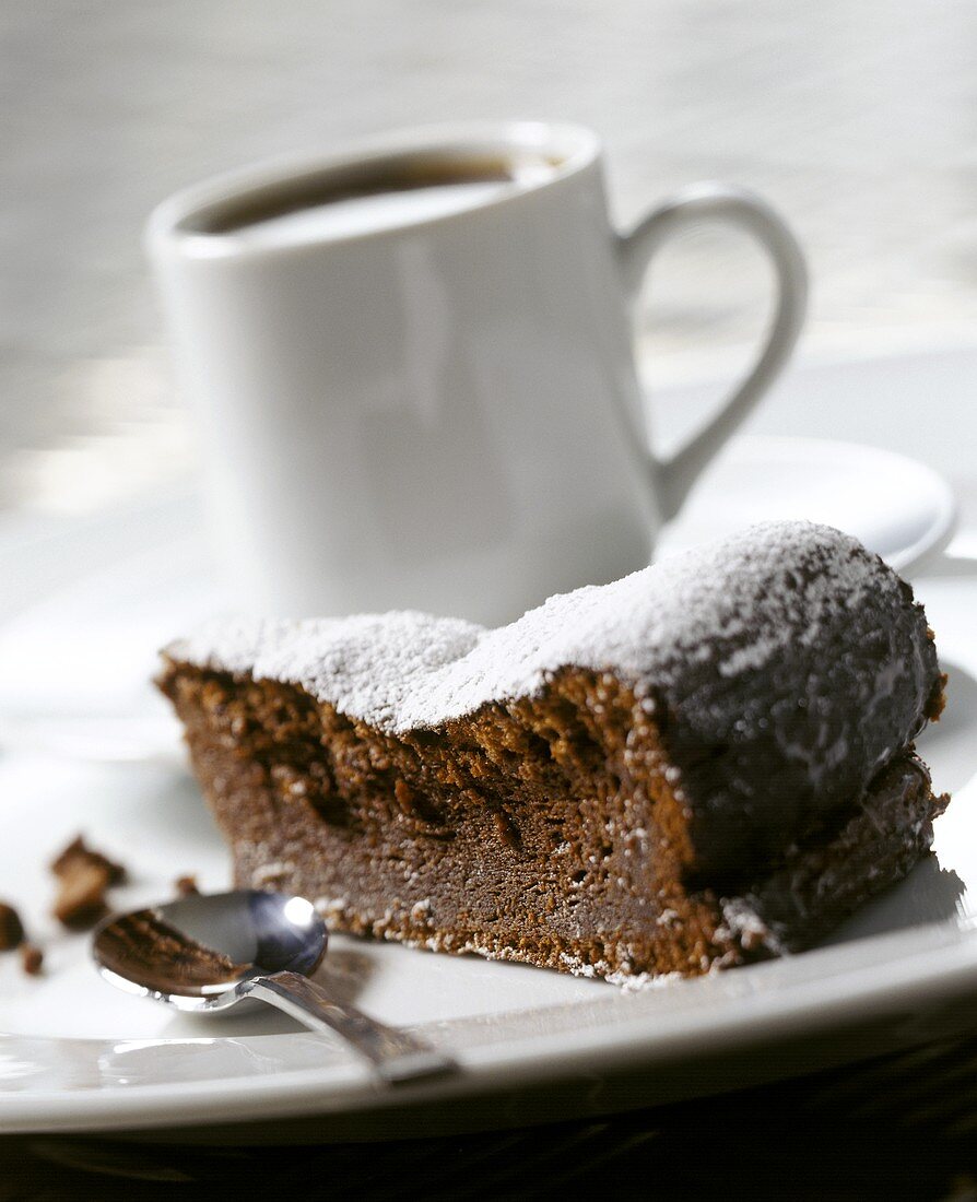 A piece of chocolate cake, a cup of coffee behind 