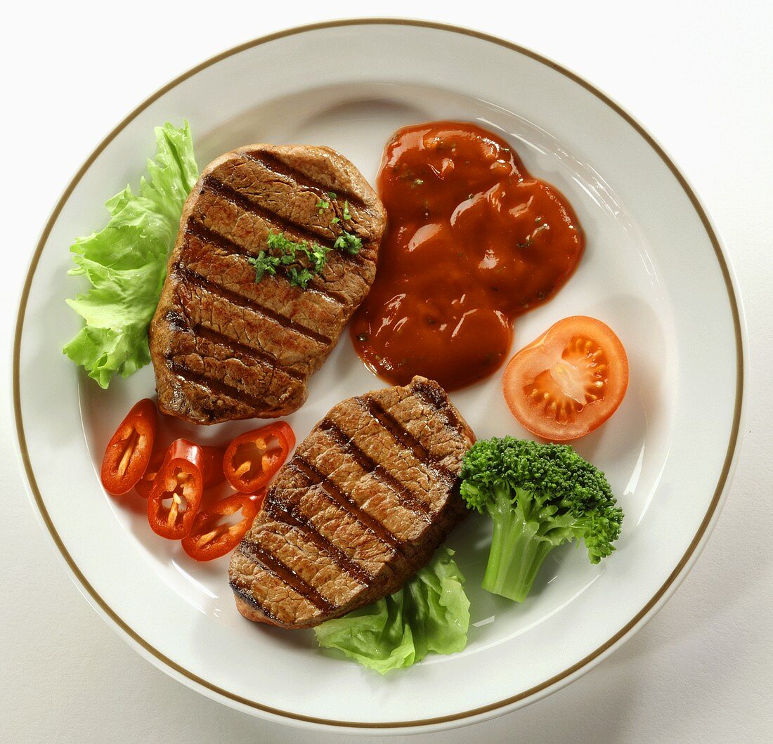 Barbecued beef steaks with vegetable garnish and ketchup