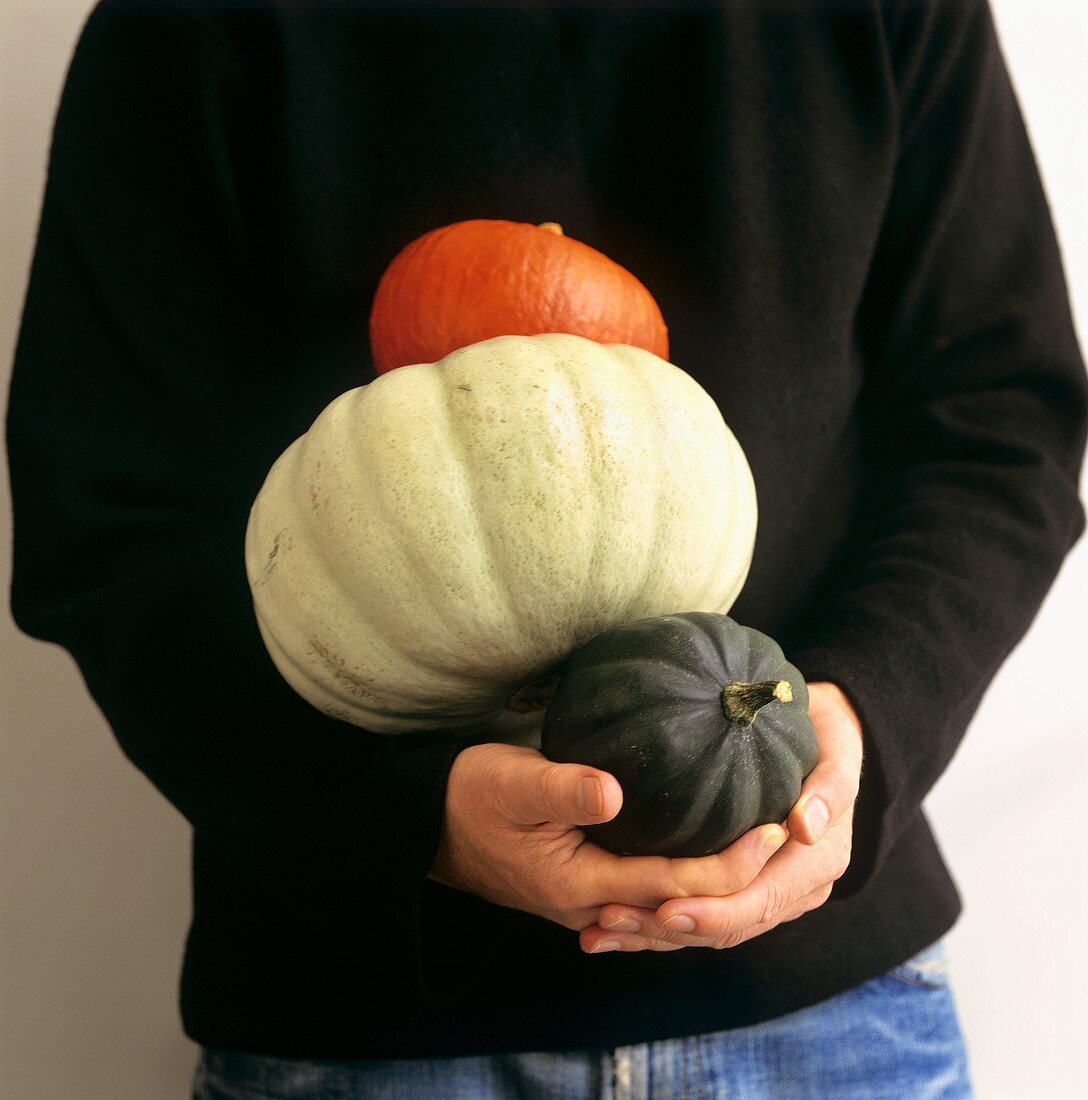 Man in black pullover holding three different pumpkins