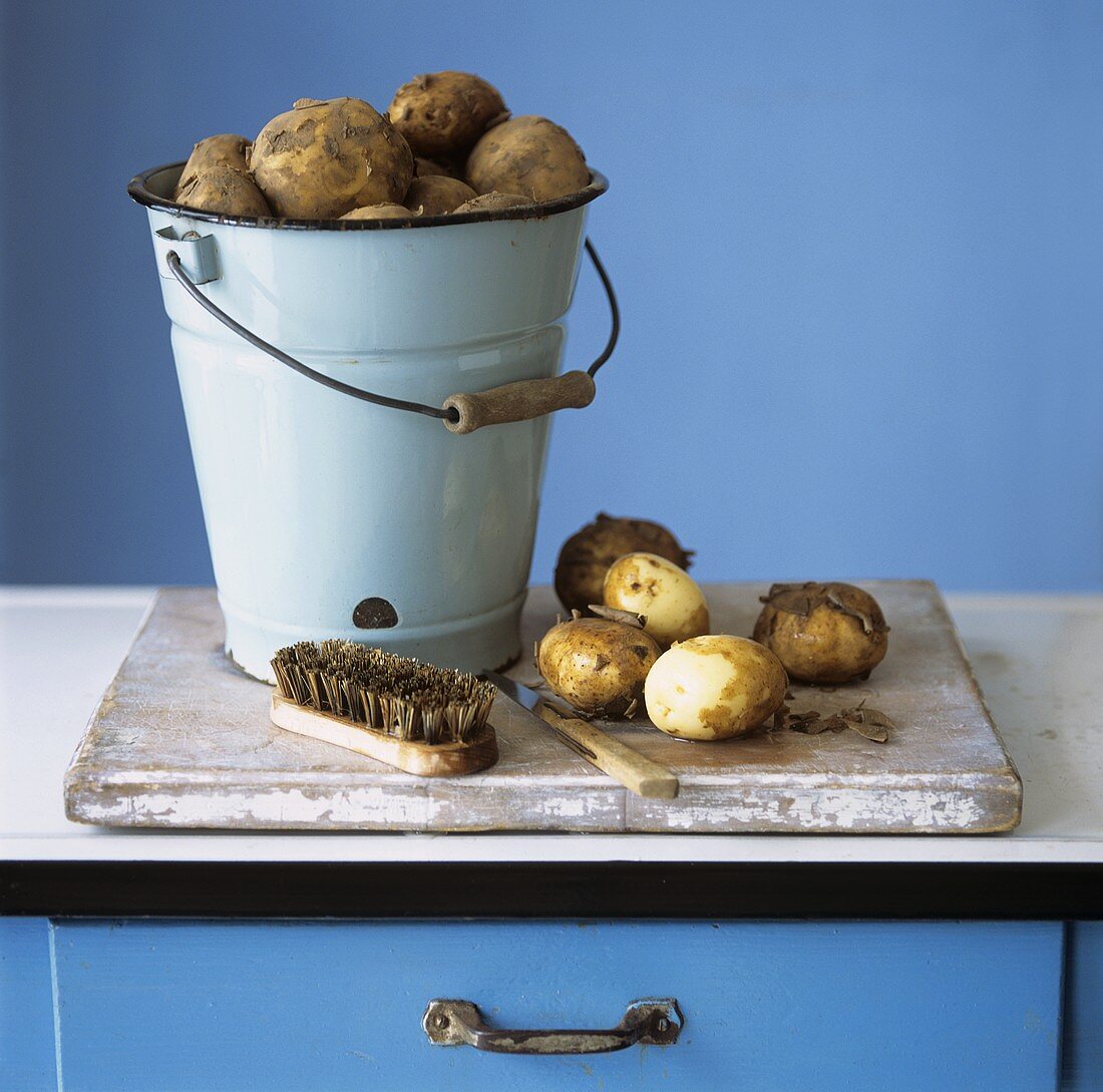 Organic potatoes in bucket and on chopping board; brush; knife