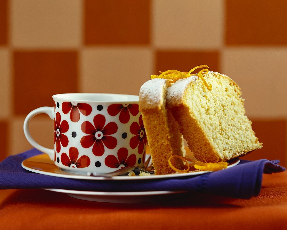 Two slices of coconut cake with orange beside coffee cup