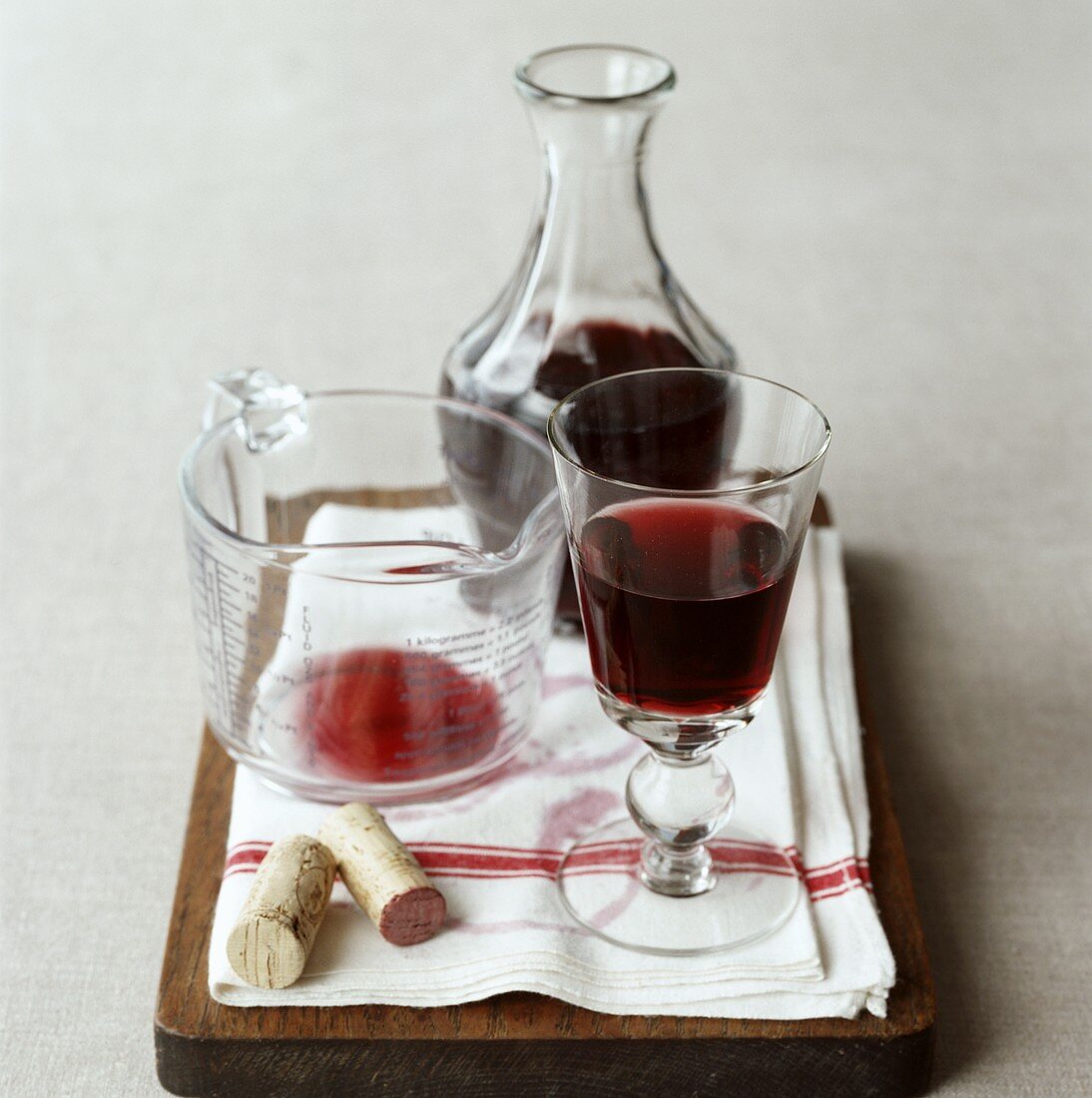Rotwein in Glas, Karaffe und Messbecher auf Schneidebrett