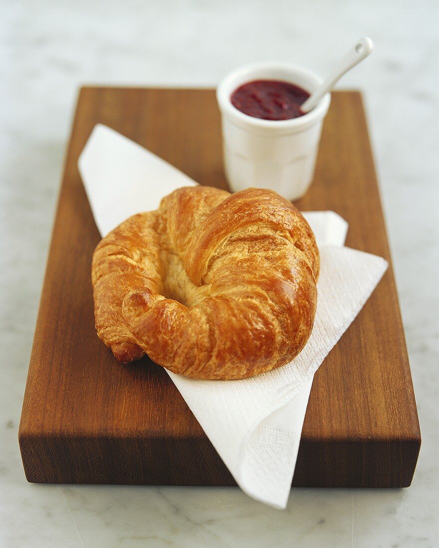 Croissant on paper napkin; strawberry jam
