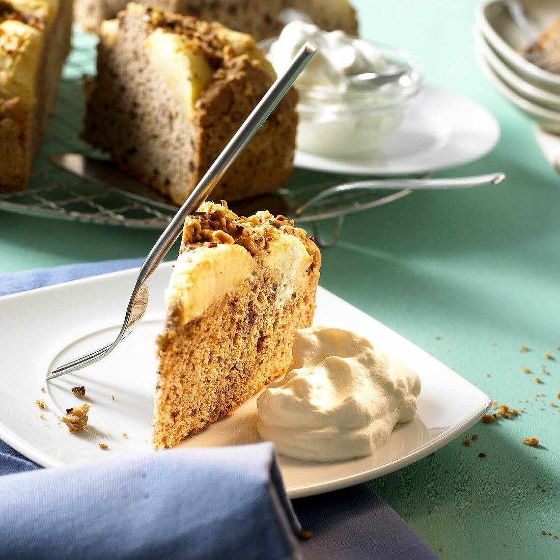 Stück warmer Apfelkuchen mit Sahne vor angeschnittenem Kuchen