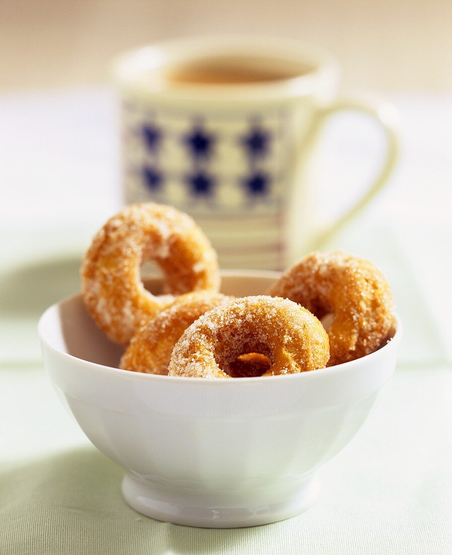 Donuts mit Zucker in weisser Schale vor Kaffeetasse
