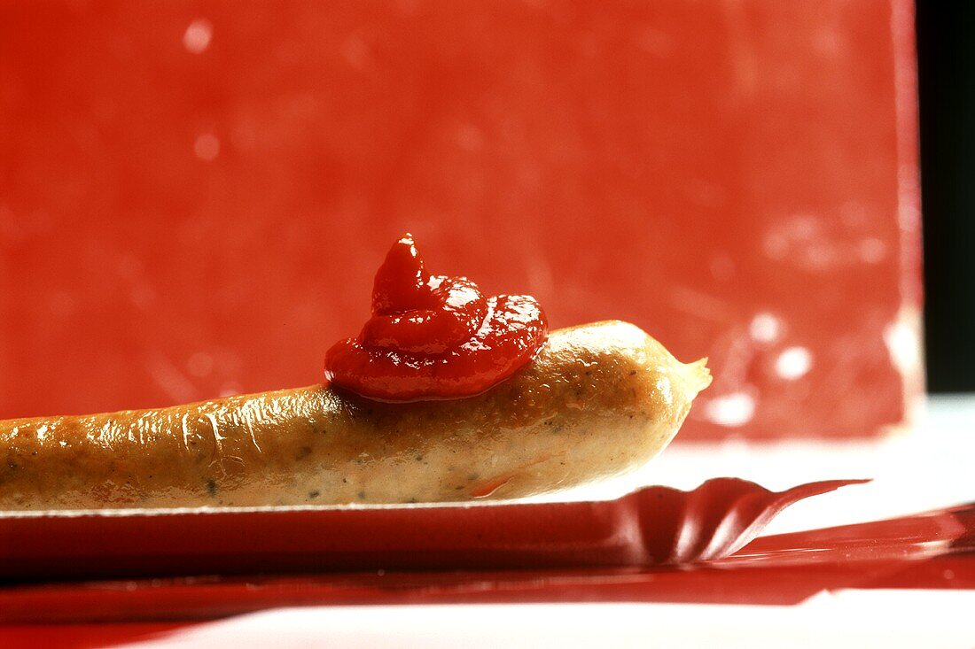 Fried sausage with ketchup on a paper plate