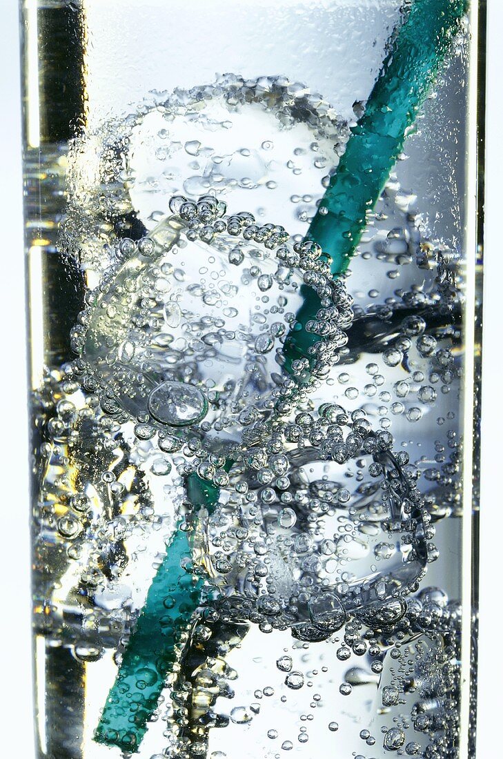 Ein Glas sprudelndes Wasser mit Eiswürfeln und Strohhalm