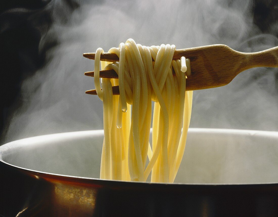 Lifting spaghetti out of steaming pan with wooden fork