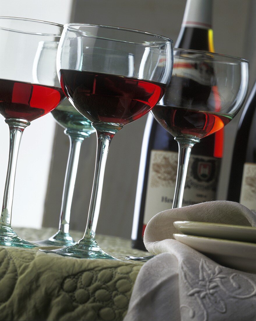 Drei Gläser Rotwein, dahinter Rotweinflasche