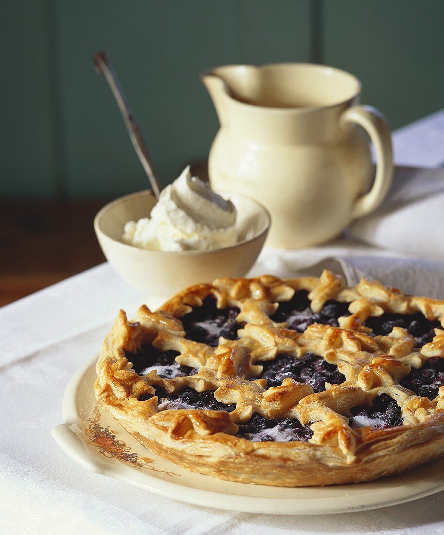 A blueberry tart with a bowl of whipped cream beside it