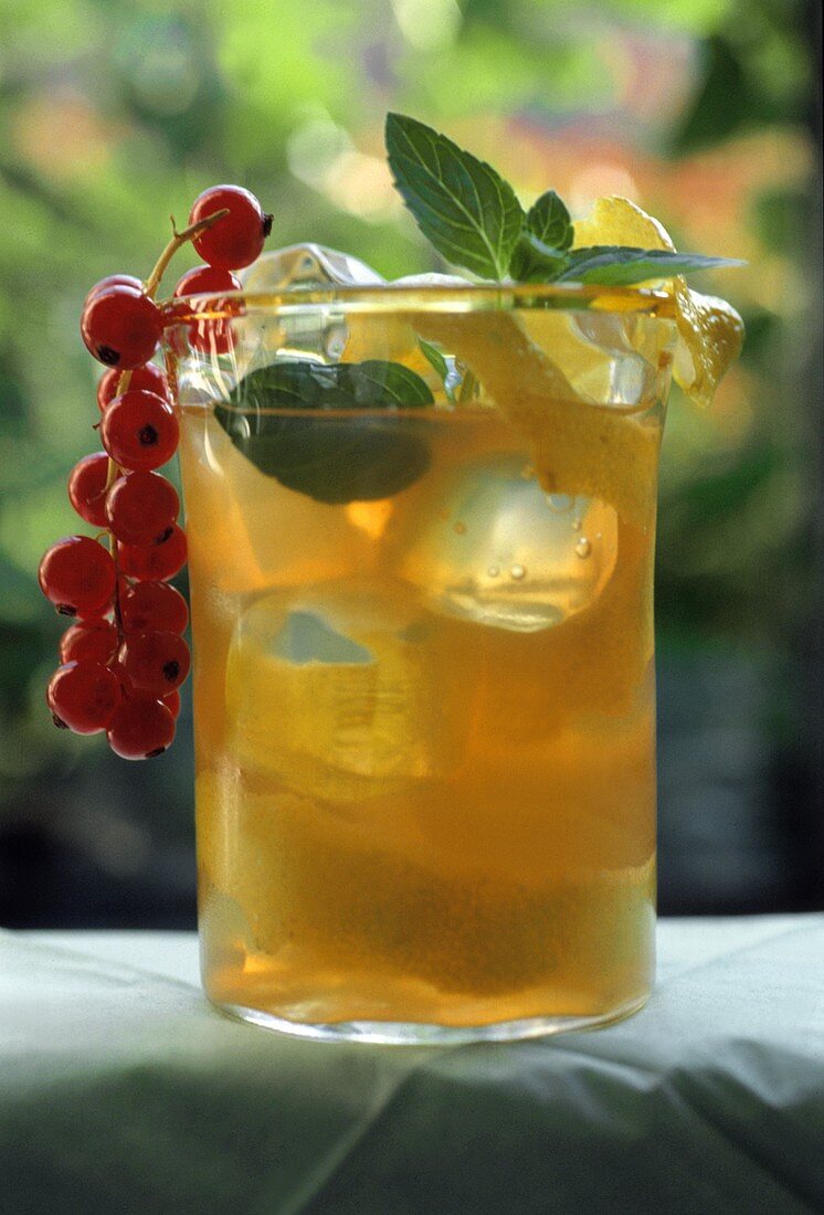 A glass of iced tea with mint leaves and redcurrants