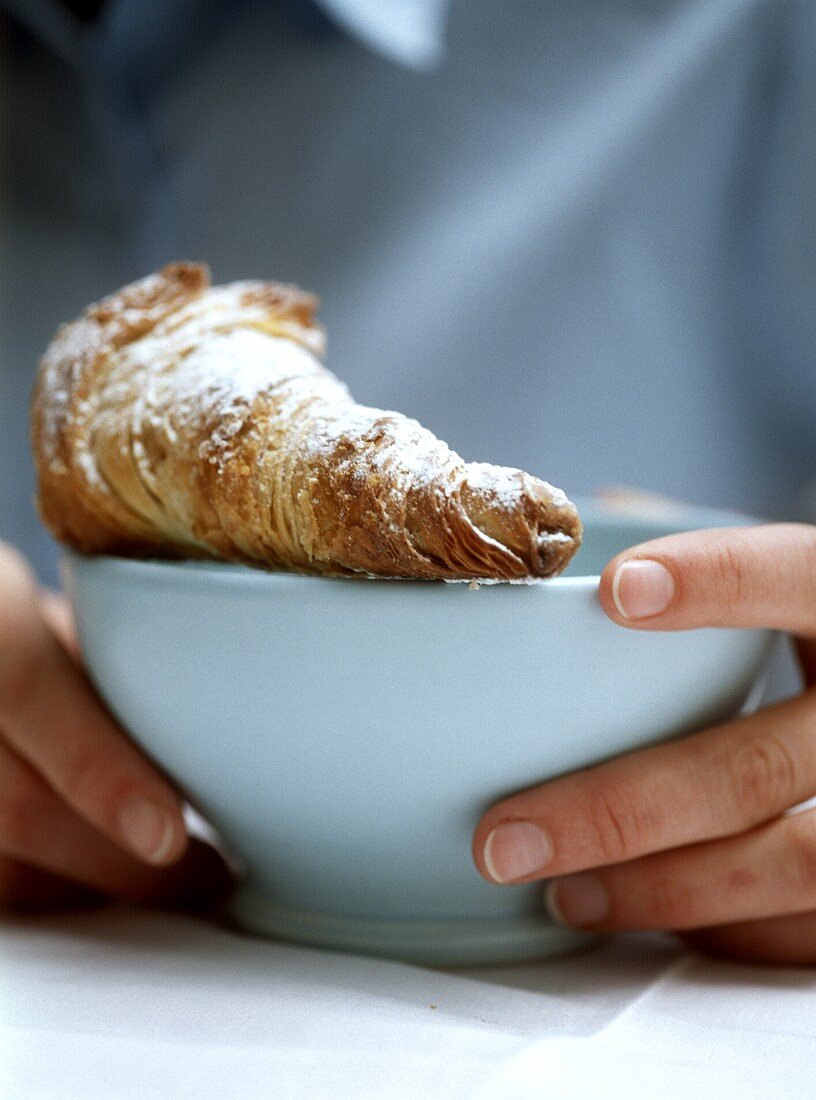 Hände halten Schälchen mit Croissant