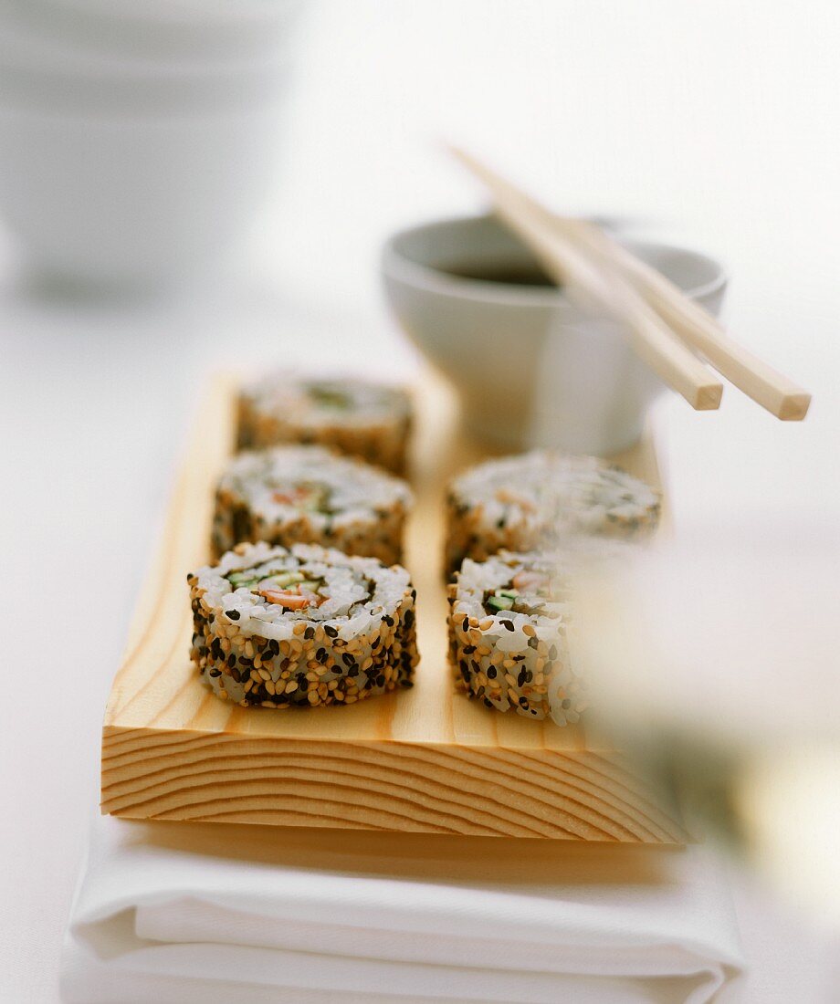 Sesam-Sushi auf Holzbrett, dahinter Sojadip