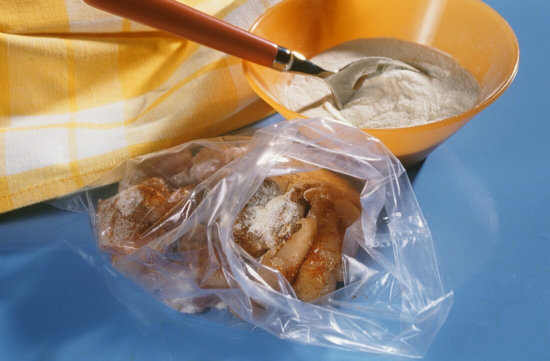 Strips of meat with seasonings and flour in plastic bag