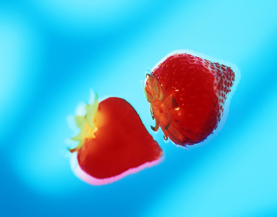 Two strawberries against blue background (surreal)