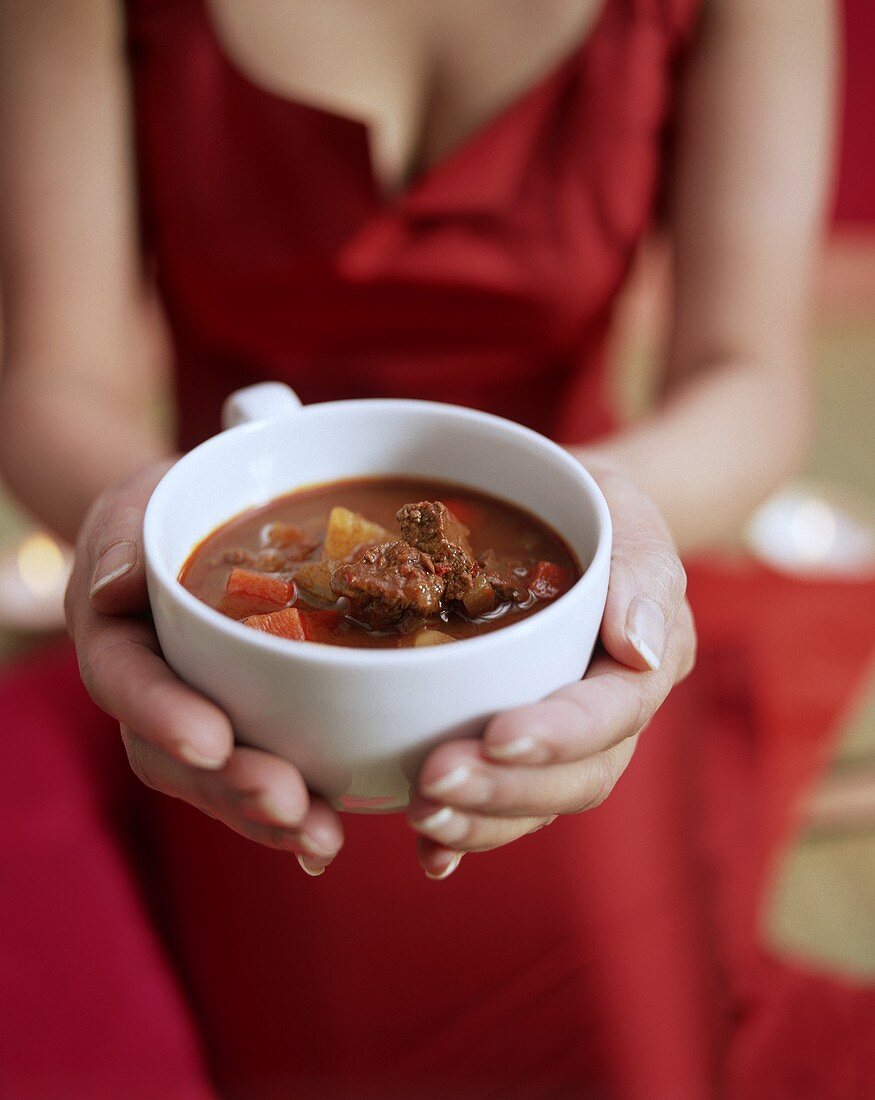 Frau im roten Kleid serviert ungarische Gulaschsuppe