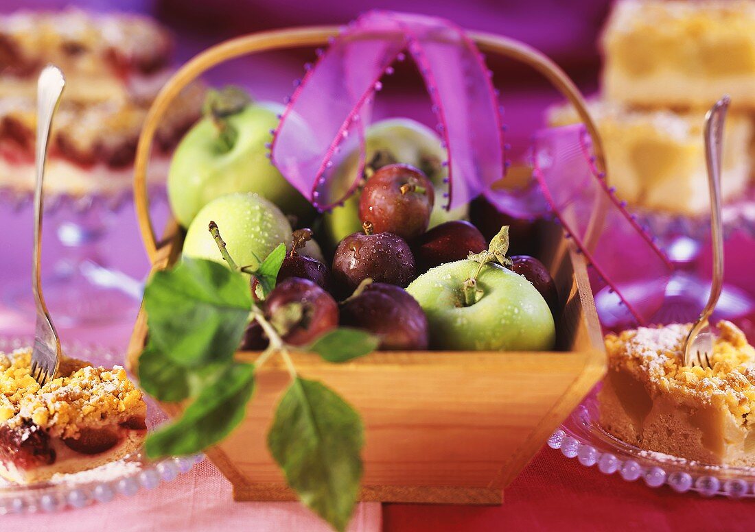 Pieces of apple cake and plum cake, fruit basket between them