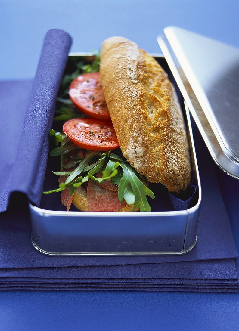 Baguette with pastrami, rocket and tomatoes in picnic box