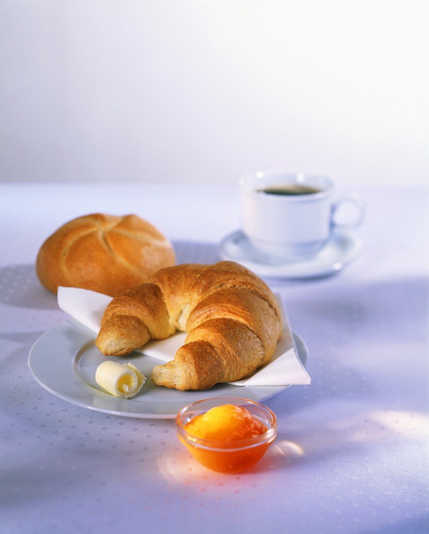 Breakfast of croissant, roll, jam and coffee