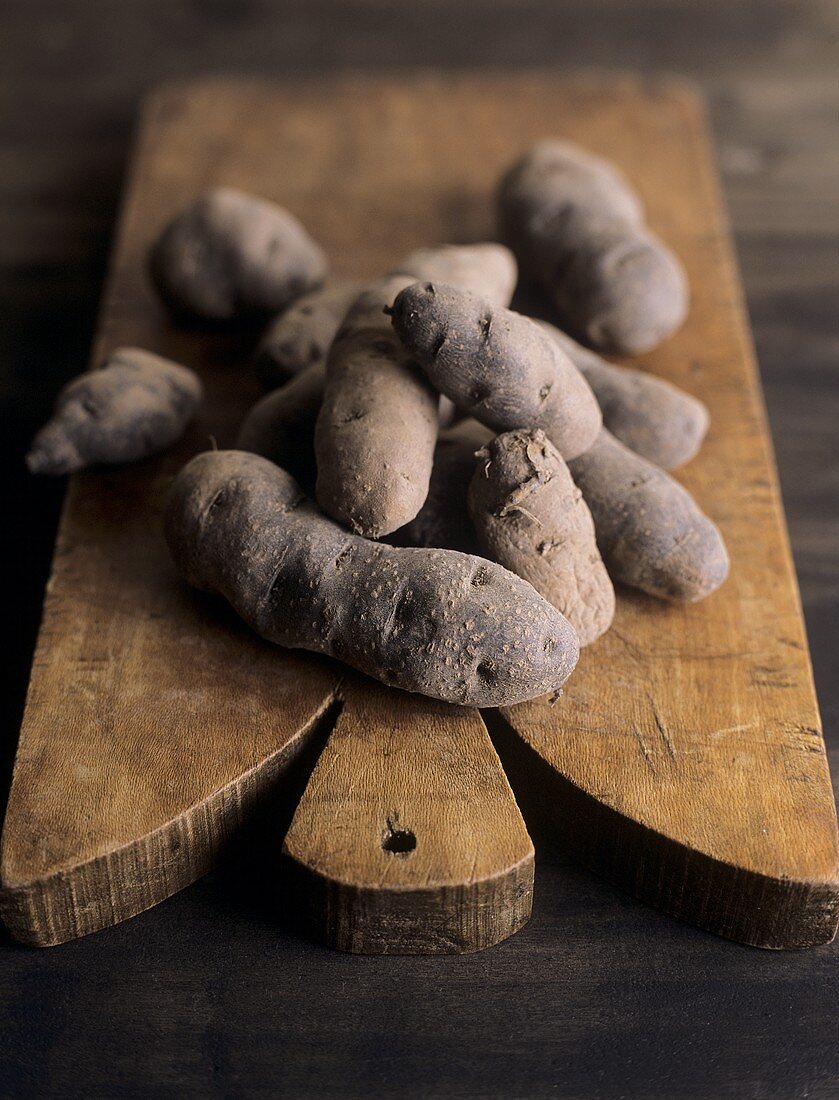 A few potatoes, Vitelotte variety, on wooden chopping board