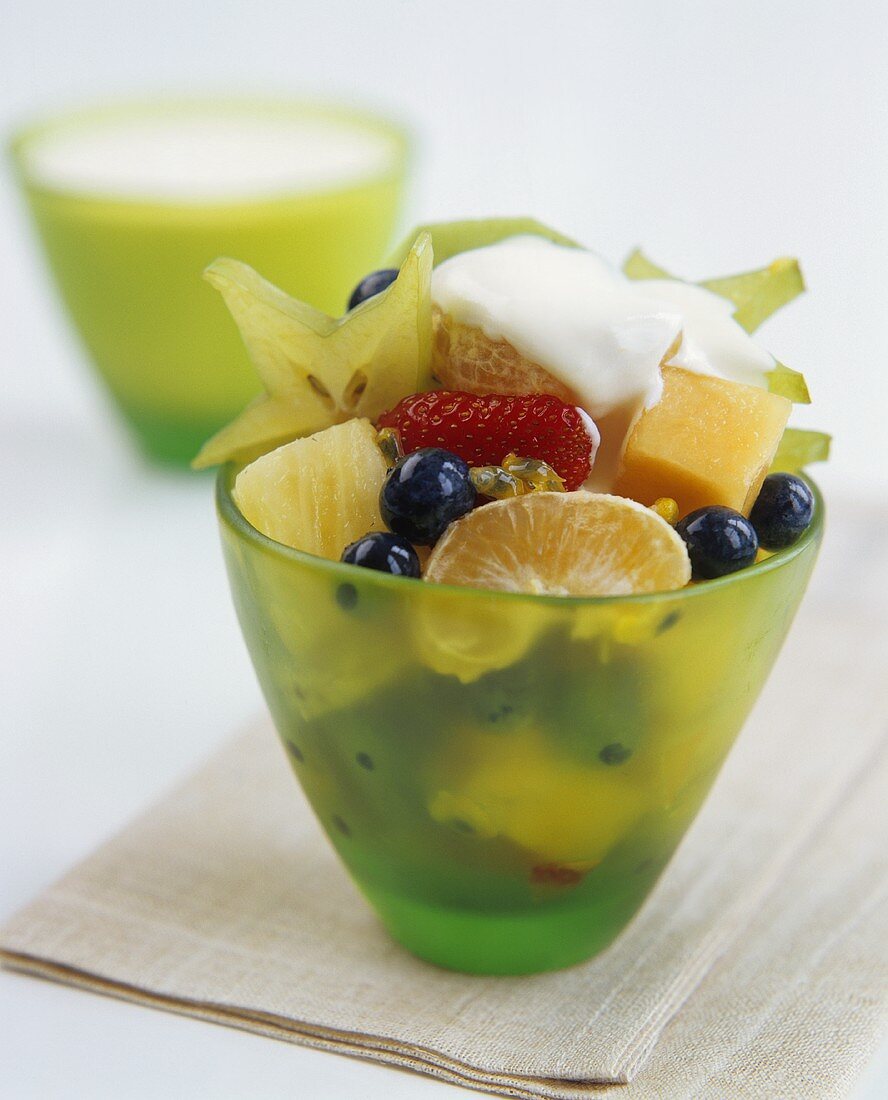 Fruit salad with a blob of cream in green glass bowl