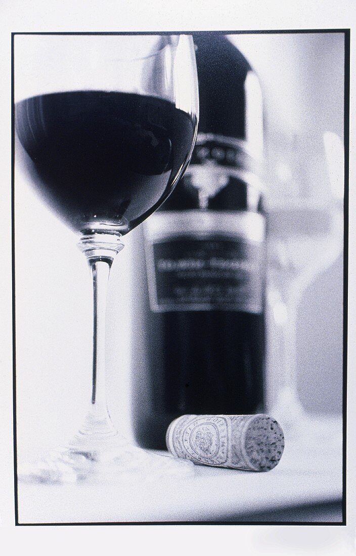 A bottle and a glass of red wine and a wine cork