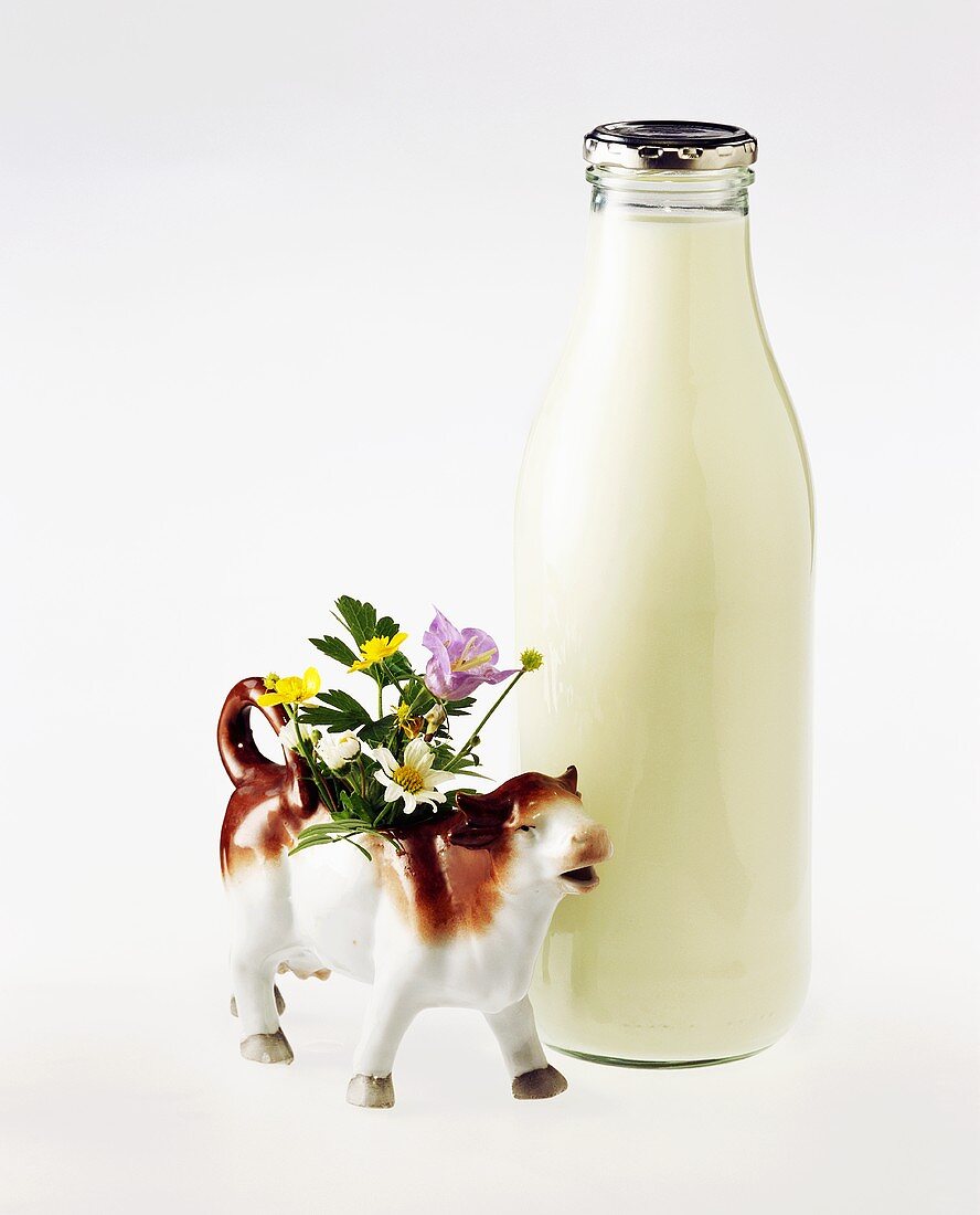 Milchflasche und Porzellankuh mit Blumen