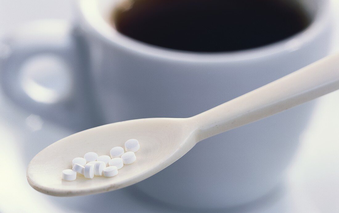 Sweetener tablets on spoon in front of coffee cup