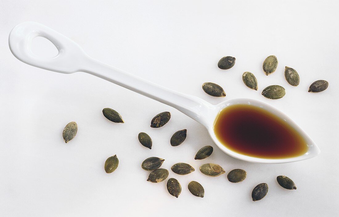 Pumpkin seed oil on spoon, surrounded by pumpkin seeds