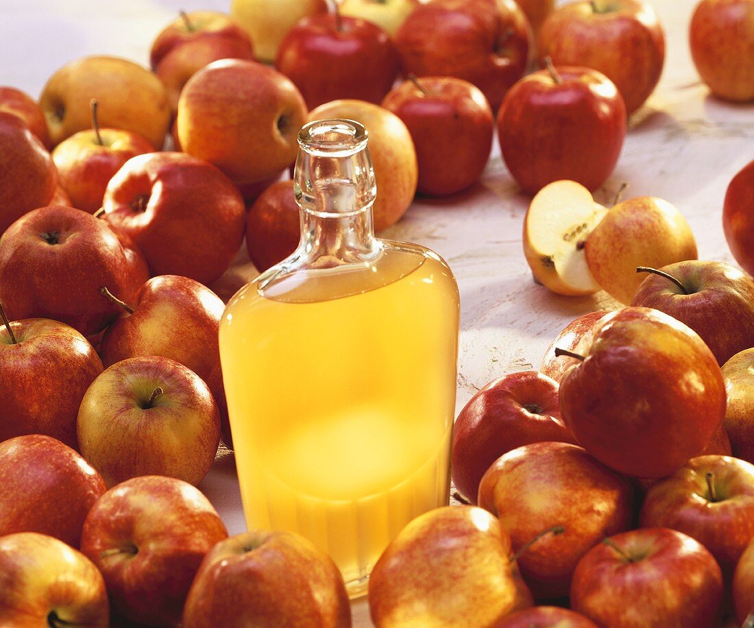 Apfelessig in Flasche, umgeben von frischen Äpfeln