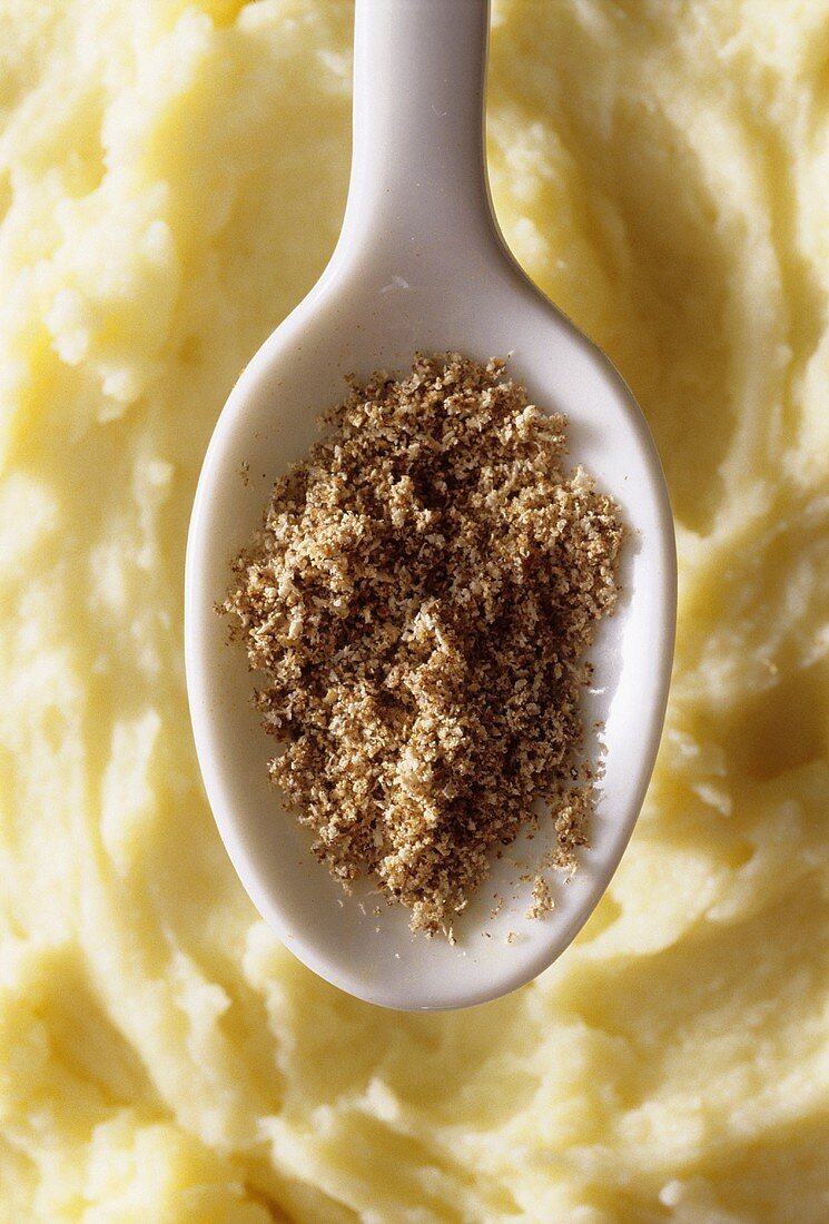 Grated nutmeg on kitchen spoon over mashed potato
