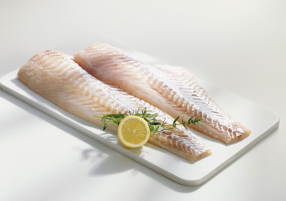 Two cod fillets on chopping board with lemon