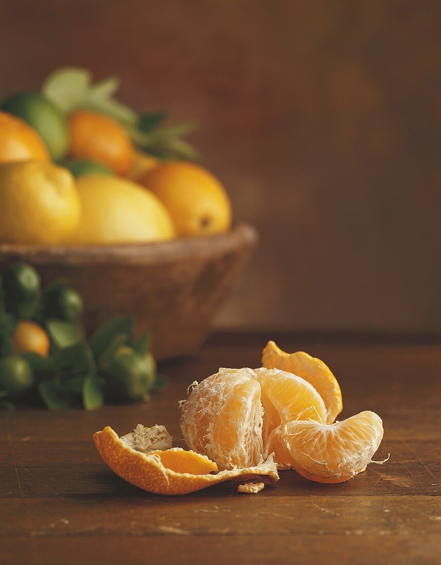 Peeled mandarin in front of basket of citrus fruit