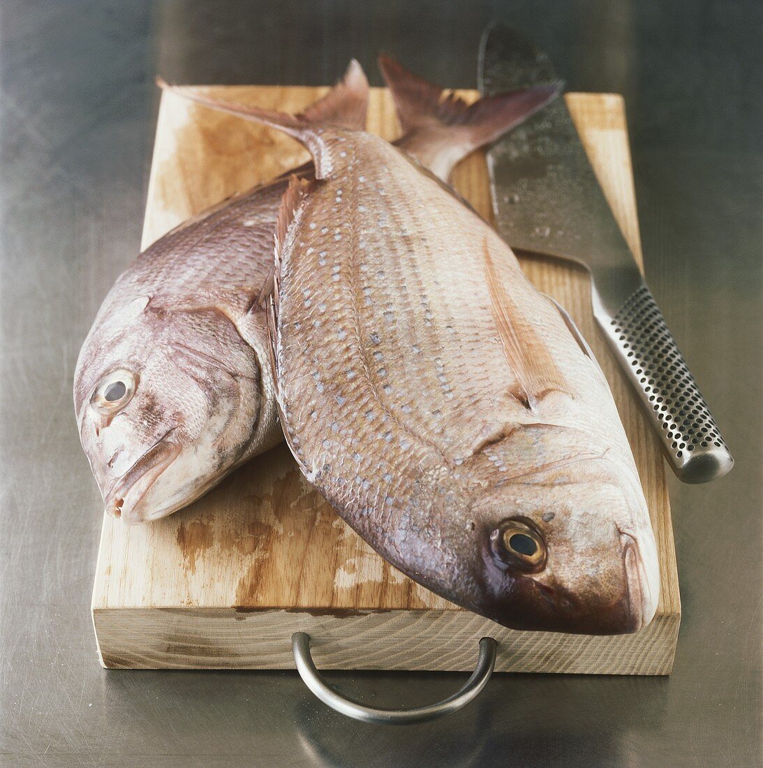 Two sea bream on chopping board with knife
