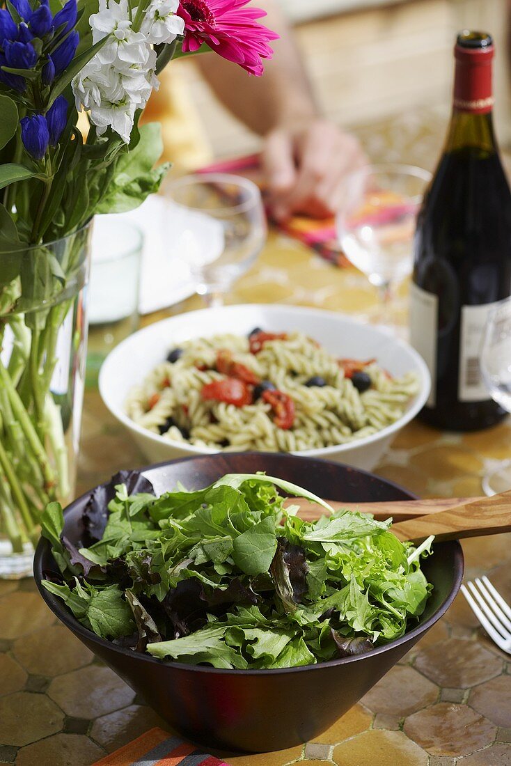 Blattsalat und Nudelsalat auf gedecktem Tisch im Freien