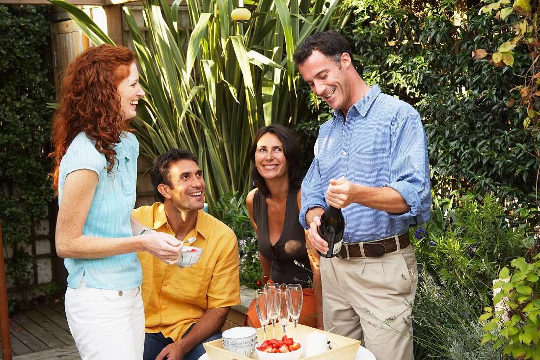 Man opening bottle of Sekt to drink with dessert at garden party