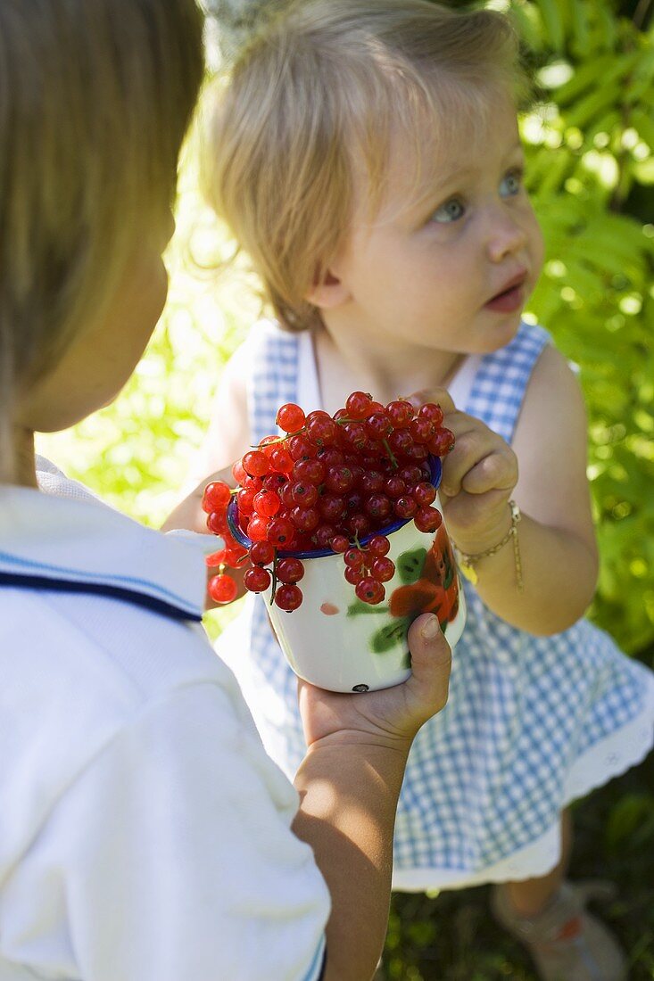 Mädchen und Junge mit roten Johannisbeeren im Freien