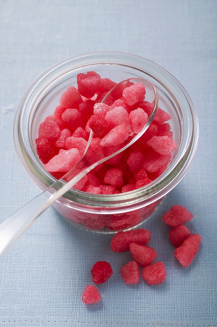 Kleine rosa Zuckerbonbons im Glas mit Löffel