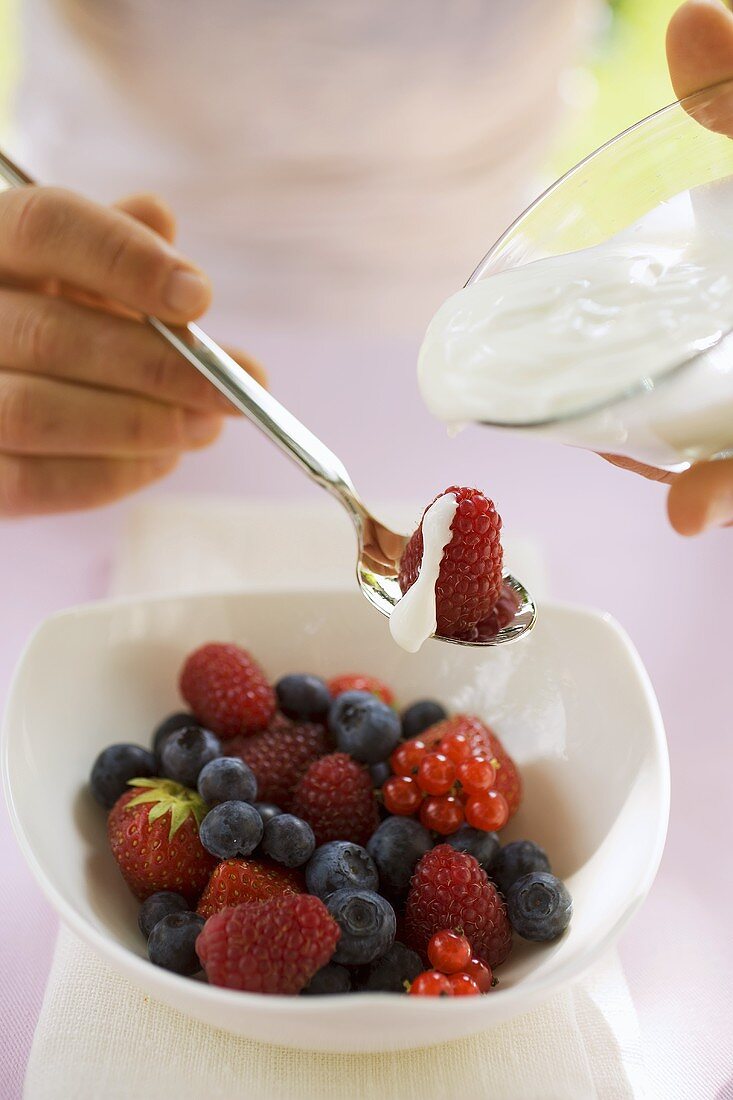 Hand giesst Joghurt auf frische Beeren