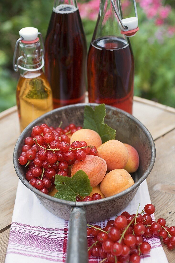 Redcurrants & apricots in pan in front of bottles of juice