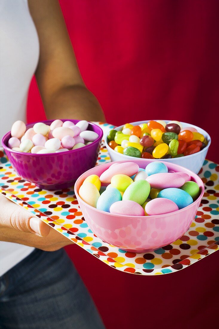 Hands holding a tray of assorted sweets in bowls