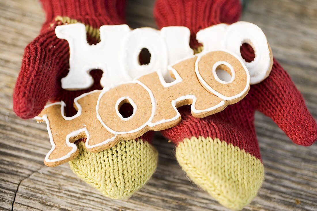 Hands in woollen mittens holding gingerbread (the word Hoho)