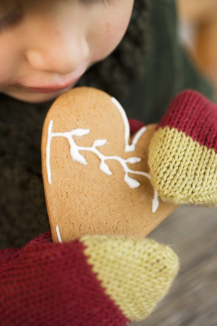 Kind mit Wollhandschuhen hält weihnachtliches Lebkuchenherz