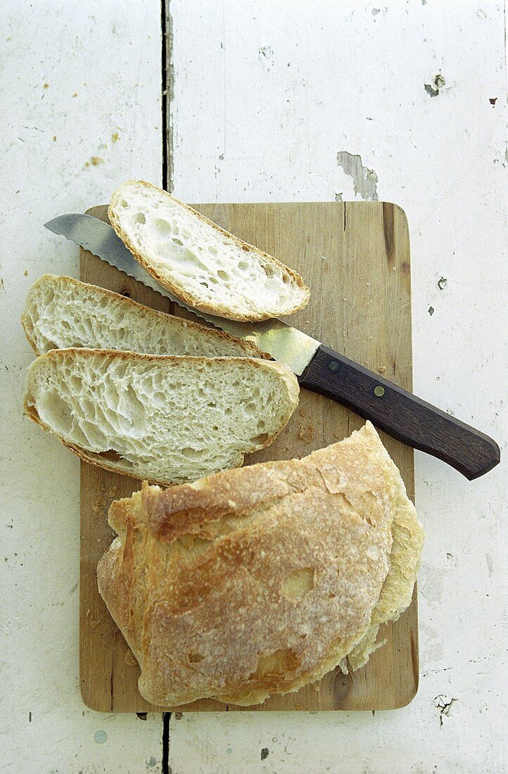 Rustic white bread, partly sliced, on chopping board